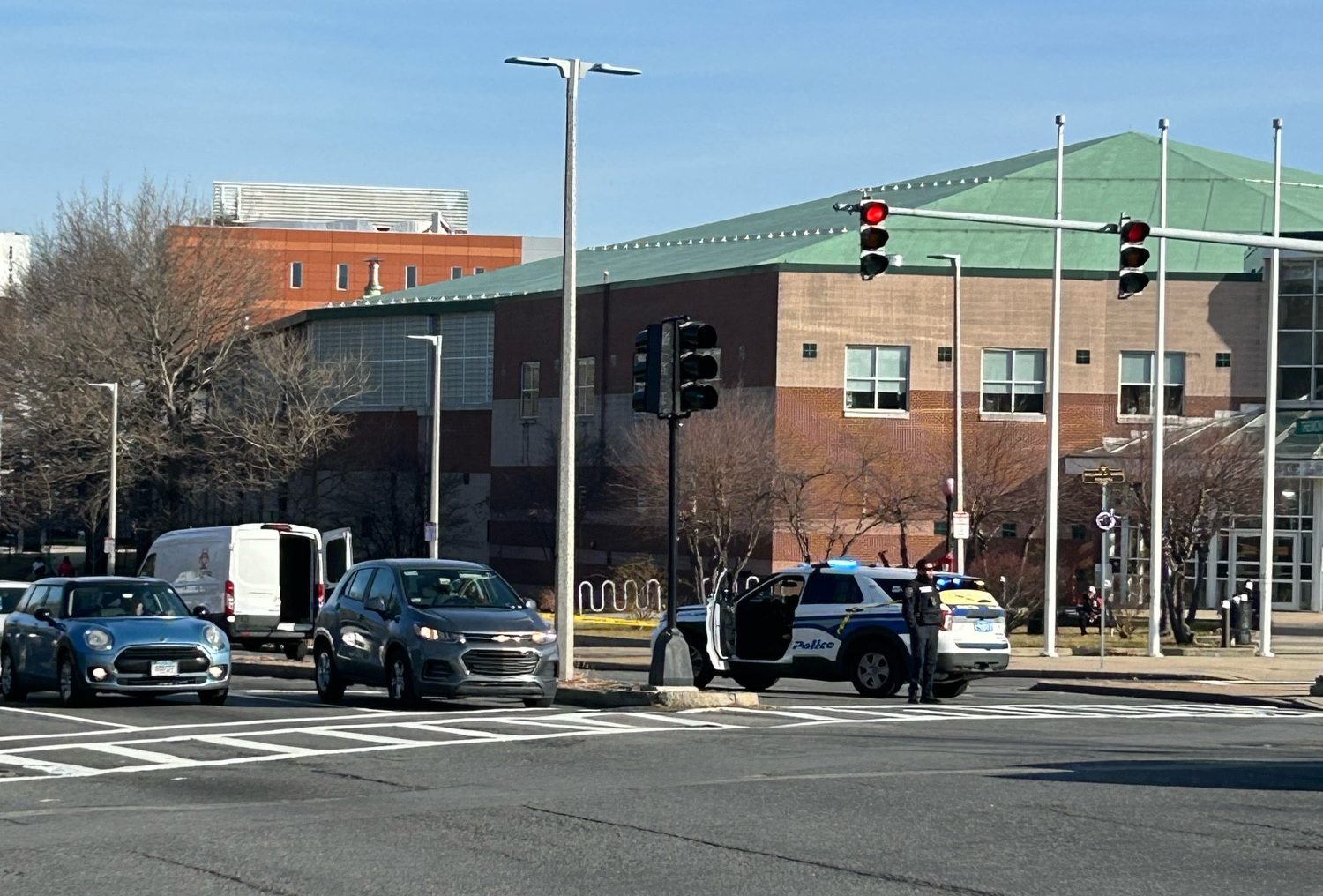 A police officer stands next to a police car parked under a traffic light in a wide multi-lane intersection